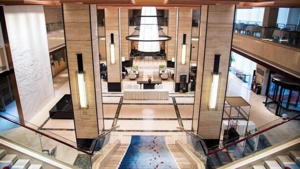 A spacious lobby with a central seating area, a staircase, and a view of the upper floors. - LOUNGE GROUP (Suzhou)