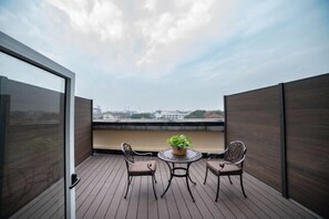 Un balcón con una mesa, dos sillas, una planta en maceta y vistas a edificios.