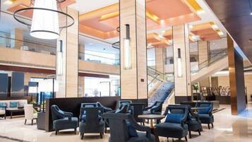 A spacious lobby with multiple seating areas, a staircase, and a high ceiling with modern lighting fixtures.