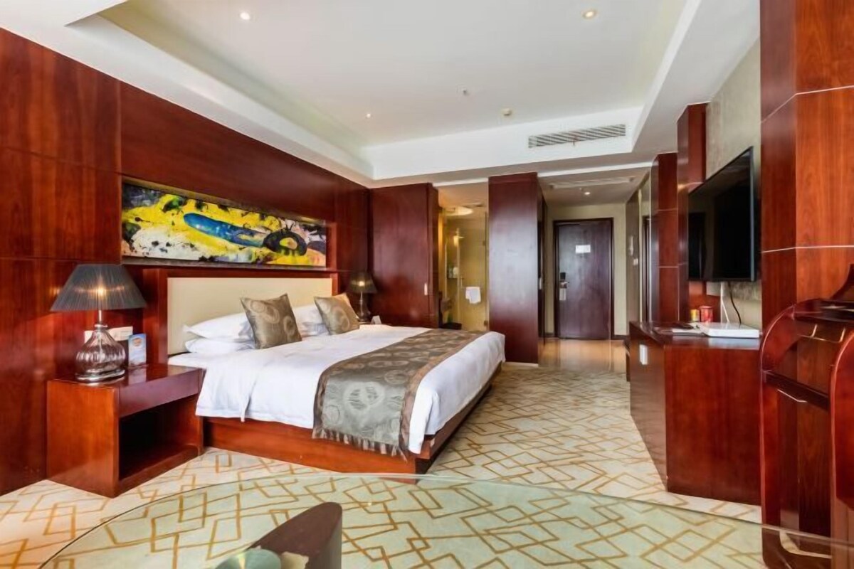 Una habitación de hotel con una cama grande, un escritorio, un televisor y un cuadro en la pared.