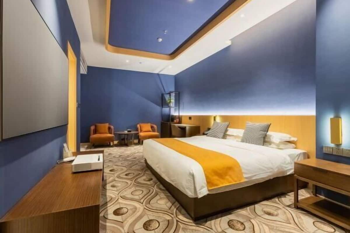 Une chambre d’hôtel moderne dotée d’un grand lit, d’un bureau et d’un coin salon avec deux fauteuils.
