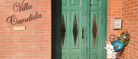 A green double door with diamond-shaped windows, a welcome sign, and a decorative vase with flowers.
