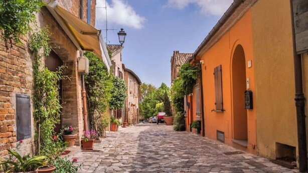 Una estrecha calle adoquinada bordeada de edificios históricos, algunos con ladrillo a la vista y otros con fachadas pintadas.