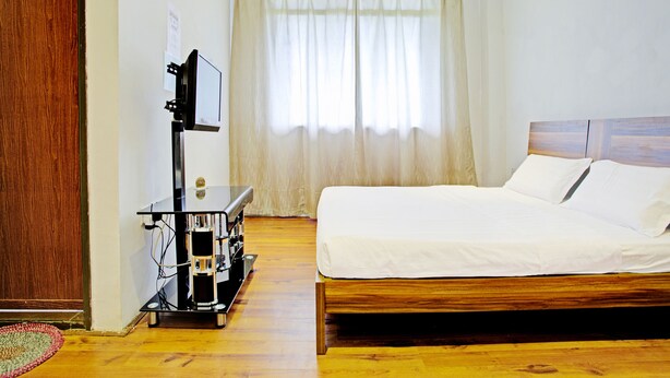 Une chambre d’hôtel avec un lit en bois, un téléviseur posé sur un meuble et une fenêtre avec des rideaux.