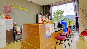 Un comptoir d’accueil avec un revêtement en bois, une enseigne indiquant « Delightful Holiday Inn », et une vue sur la verdure à l’extérieur.
