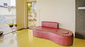 Un canapé rouge dans une pièce dont le sol est en bois, avec une horloge au mur et une fenêtre donnant sur l’extérieur.