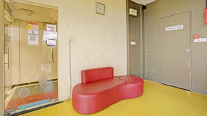 Un canapé rouge dans une pièce dont le sol est jaune, une horloge au mur et une porte portant l’inscription « Salle de conférence ».