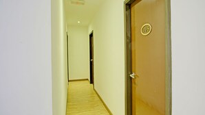 Un couloir avec un plancher en bois, une porte portant une plaque avec un numéro, et un luminaire au plafond.