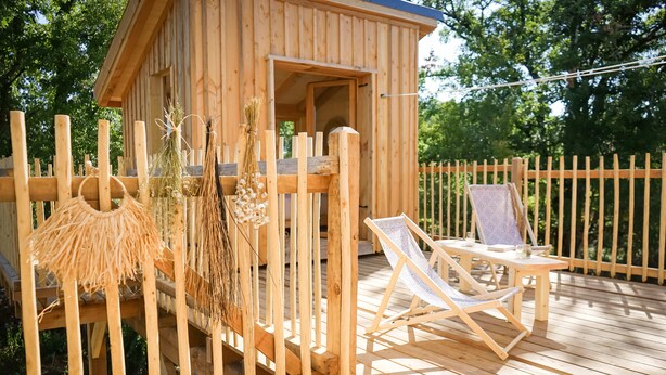Een houten hut met een terras, een lounge stoel en een kleine tafel.