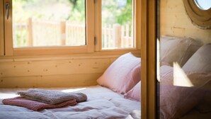 Een slaapkamer met een houten hoofdeinde, een bed met roze beddengoed en een raam met uitzicht op een houten schutting en groen.
