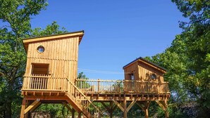 Twee houten boomhutten met balkons en een houten terras dat ze verbindt.