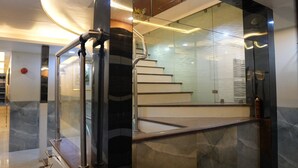 Een modern interieur met een glazen lift, marmeren vloeren en een trap met een metalen leuning.