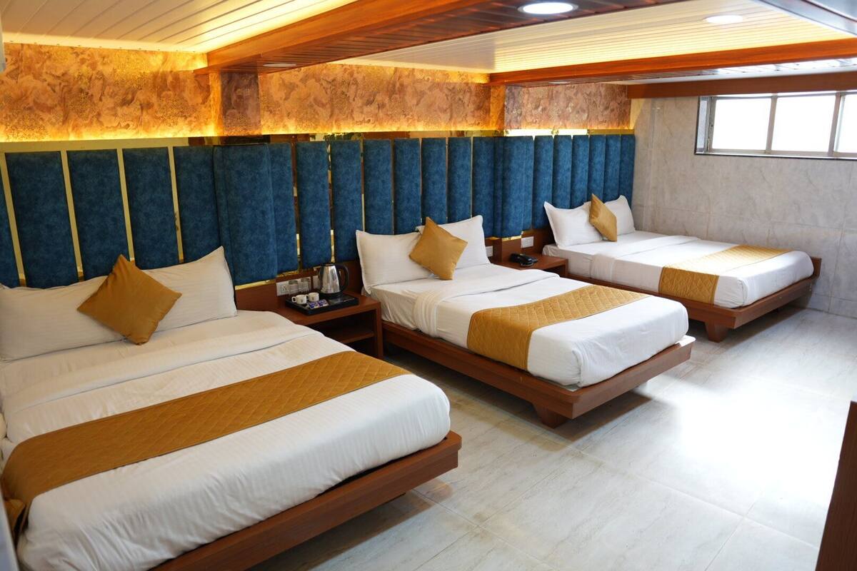 A hotel room with three beds, each with white bedding and brown accents, wooden headboards, and a stone accent wall.
