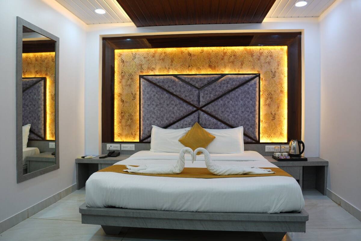 A modern hotel room with a large bed, a headboard with a geometric pattern, and a mirror on the wall.