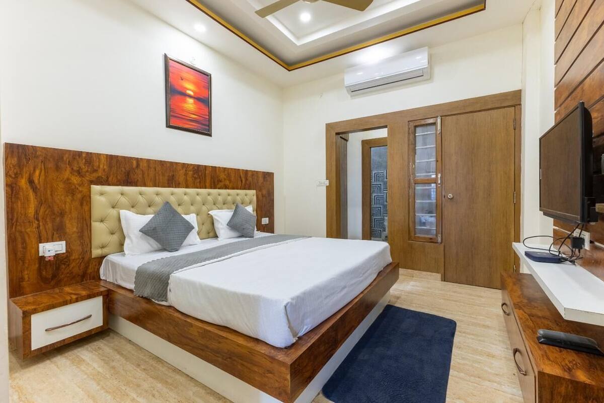 A bedroom with a wooden headboard, a bed with white bedding, a nightstand, a TV, and a wardrobe.