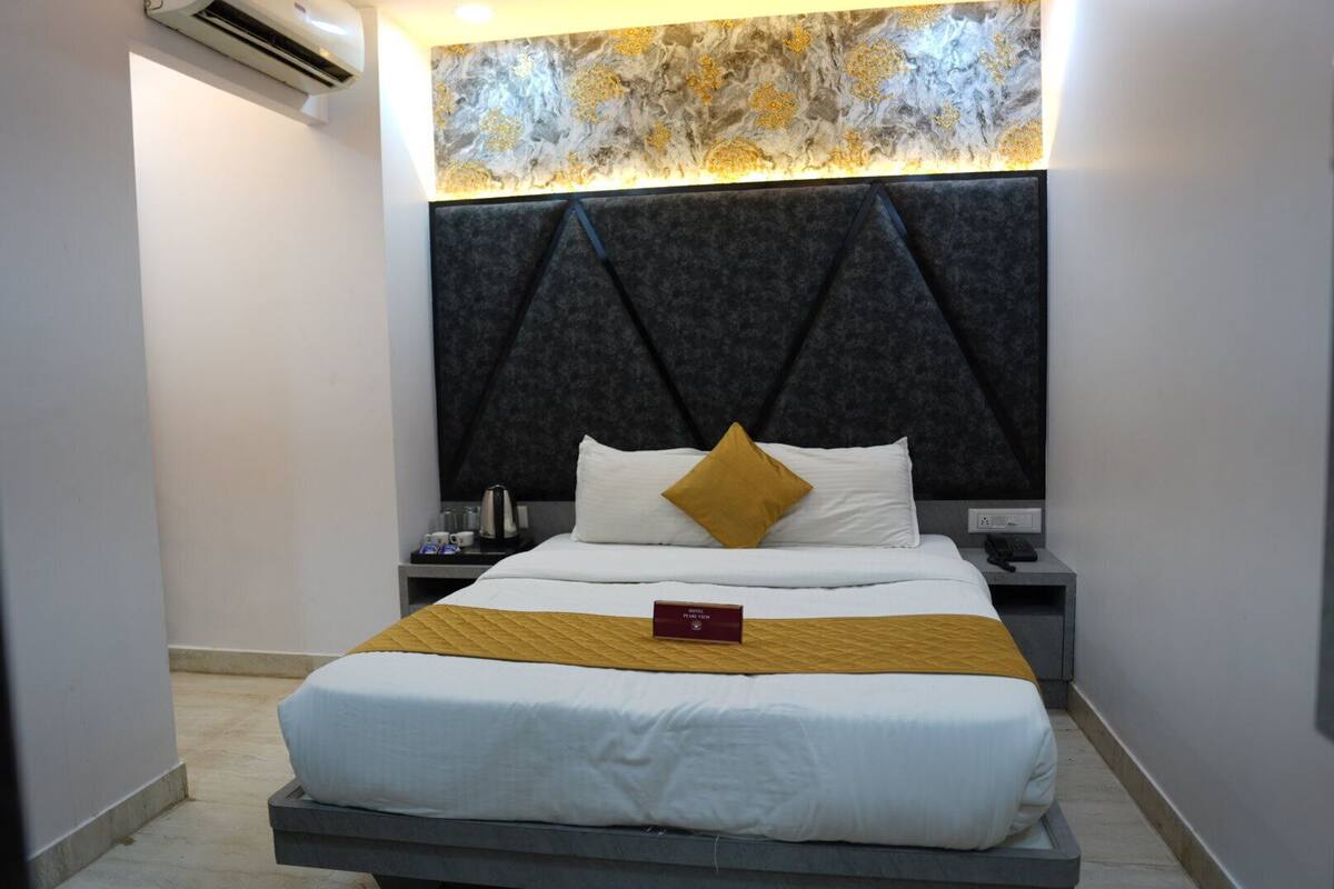 A modern hotel room with a bed, a nightstand, a wall-mounted air conditioner, and a decorative wall panel above the bed.