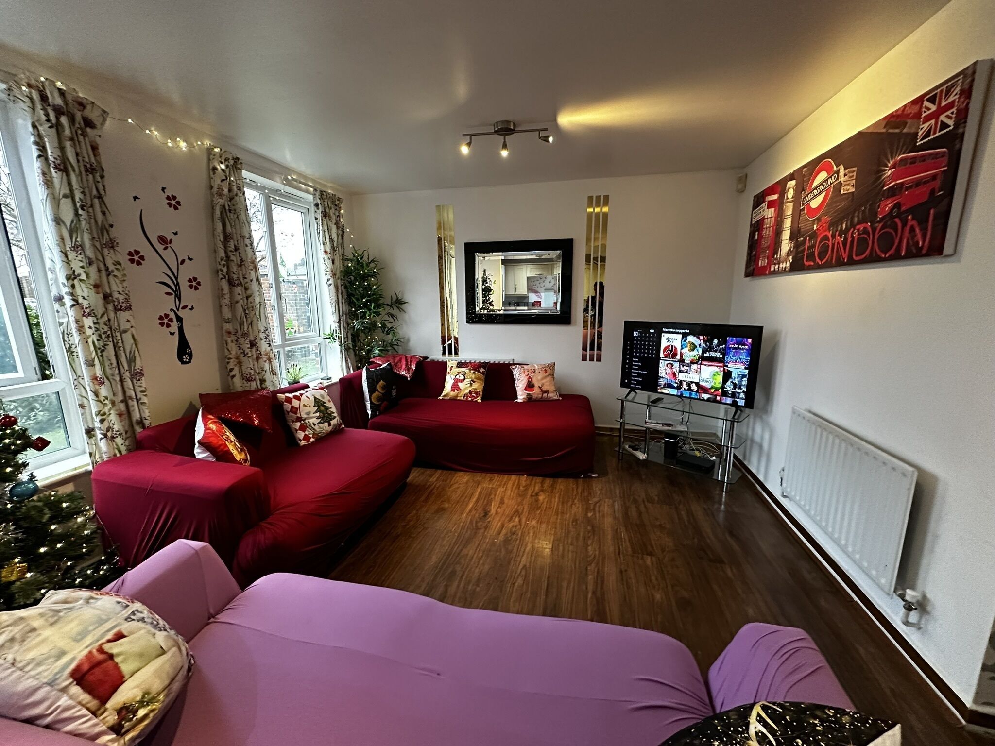 Un salon avec un canapé rouge, un canapé violet, une télévision et un sapin de Noël.