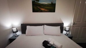 Ein ordentlich bezogenes Bett mit weißen Leinen, zwei Kissen und einem gefalteten Handtuch. Auf beiden Seiten des Bettes stehen jeweils Nachttischlampen.