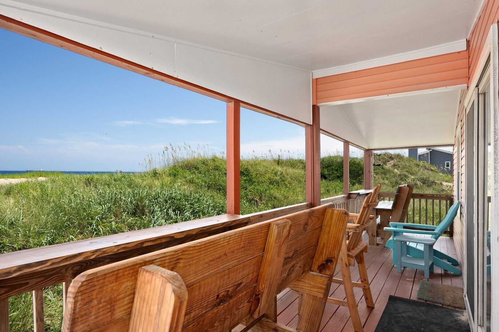 Een houten terras met stoelen met uitzicht op een strand.