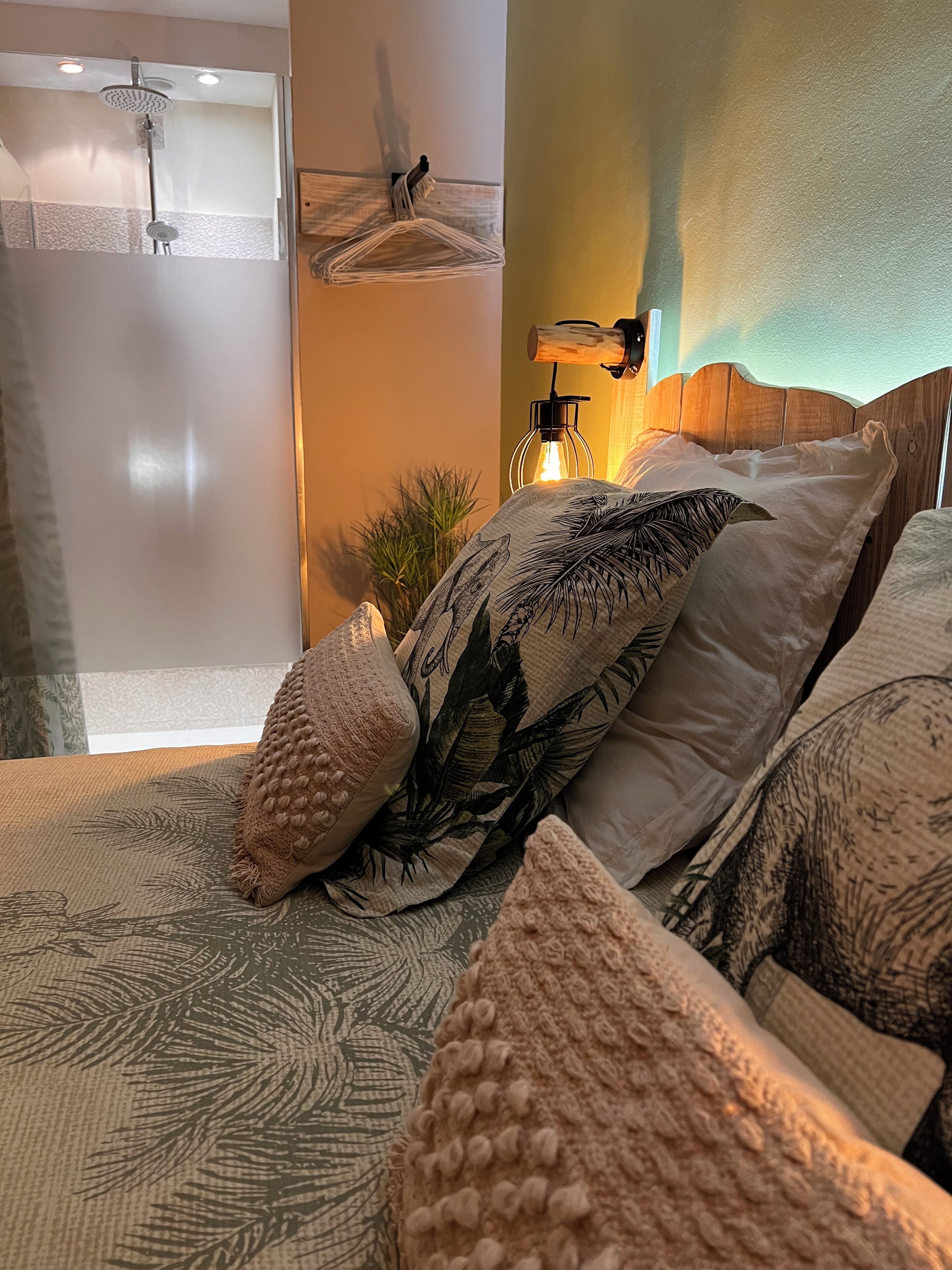 Une chambre à coucher avec un lit, des oreillers, une table de chevet, une lampe et un espace douche.