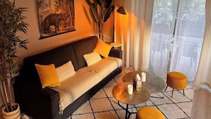A living room with a sofa, a coffee table, and a lamp. There is a painting on the wall and a window with curtains.