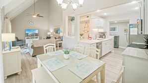 Una cocina moderna con armarios blancos, una isla central y un comedor con mesa y sillas.