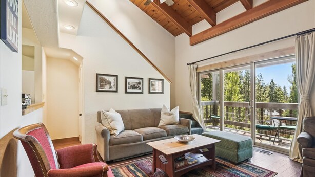 A cozy living room with a wooden ceiling, a sofa, a red armchair, a coffee table, and a large window with a view of trees.