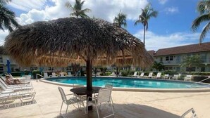Area piscina con sedie a sdraio, un tavolo e un ombrellone di paglia.