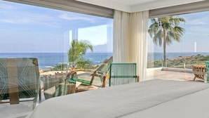 Un dormitorio con una cama grande, vista al océano y un balcón con sillas y una mesa.