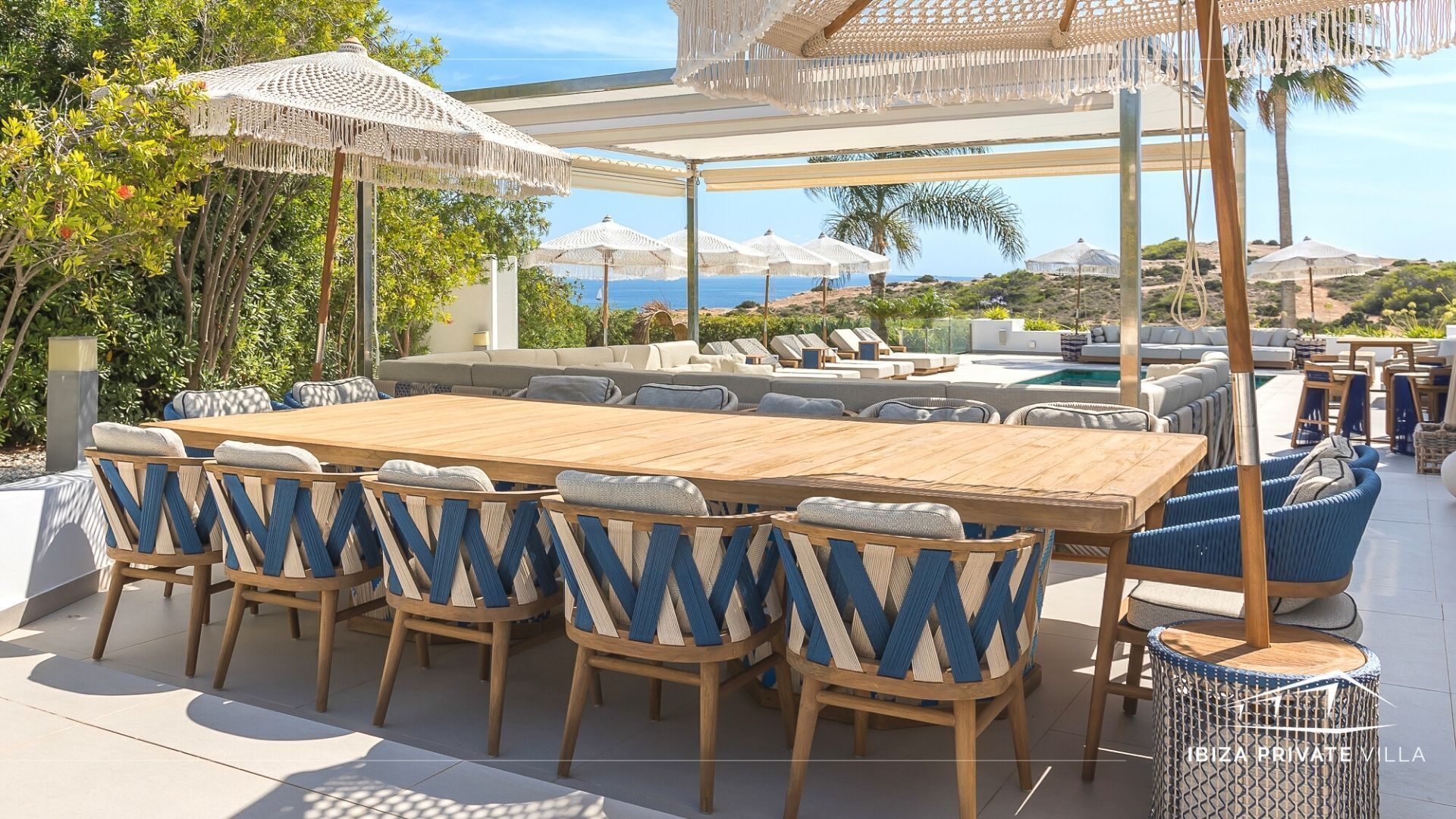 A covered outdoor dining area with a wooden table and chairs, surrounded by umbrellas and seating.