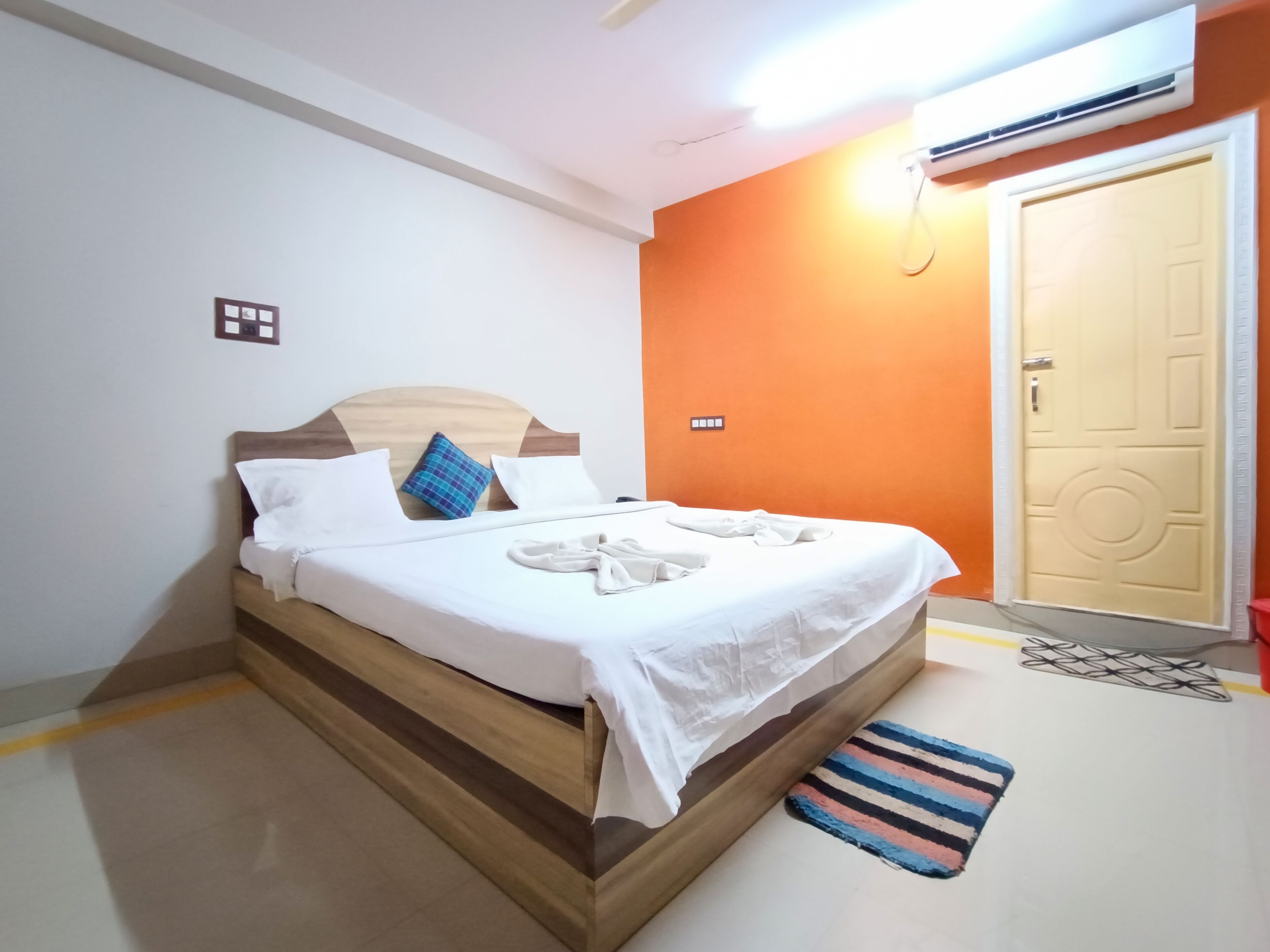 A neatly made bed with white linens and a blue and red striped rug at the foot of the bed.
