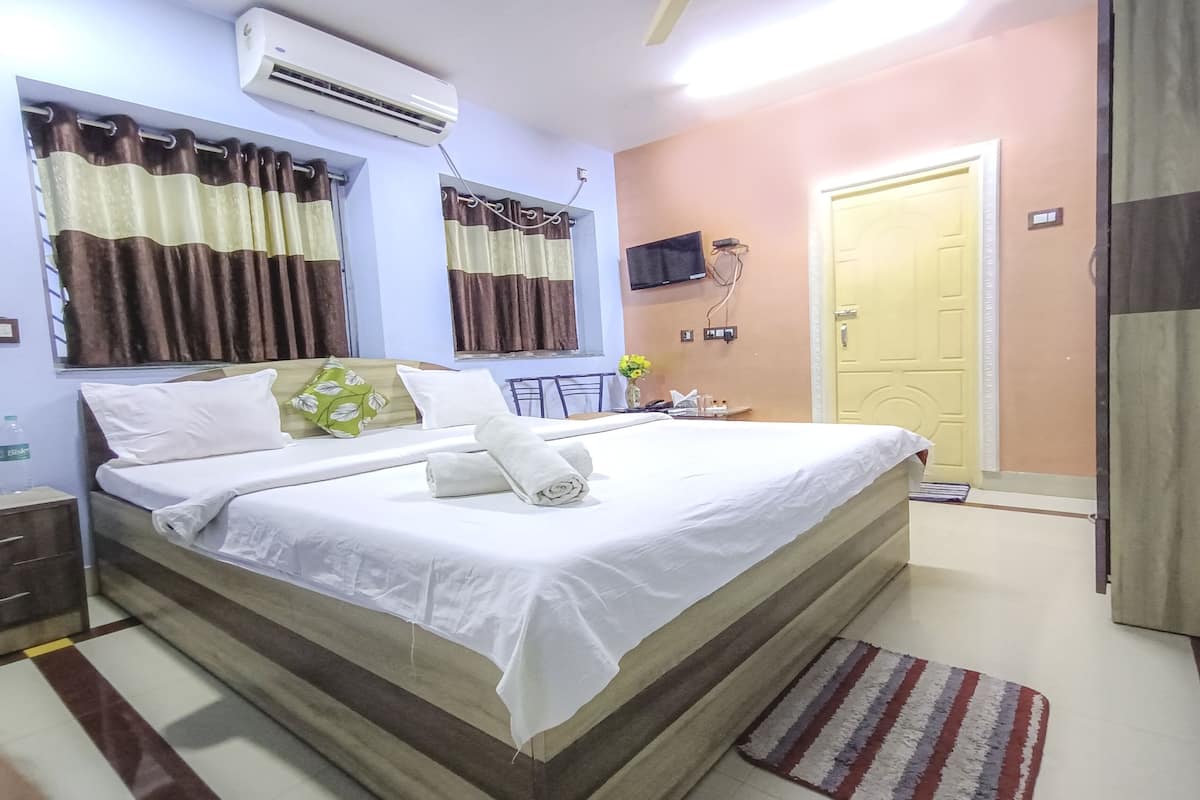A hotel room with a large bed, a bedside table, an air conditioner, a TV, and a door.