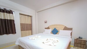 A neatly made bed with white linens and towels, a wooden headboard, and a bedside table with a phone.