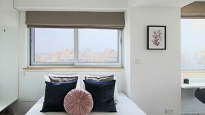 A bedroom with a large window, a bed with pillows, a framed picture on the wall, and a desk with a chair. - Phaedrus Living Luxury Suite Nicosia 507 (Strovolos)
