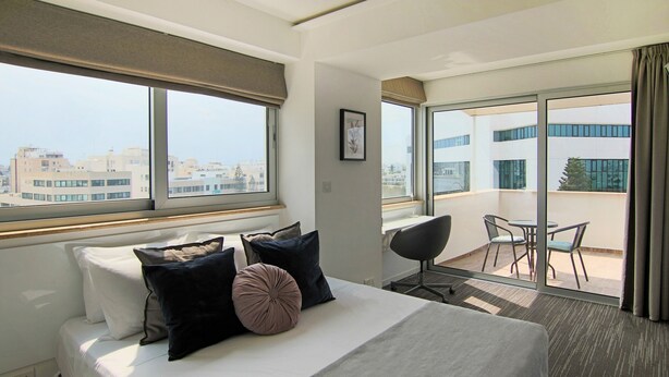 A hotel room with a bed, a desk, and a balcony with a table and chairs. - Phaedrus Living Luxury Suite Nicosia 507 (Strovolos)