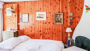 A room with wooden panel walls, a bed with white linens, a small bedside table with a lamp, and a chair. - Olympic F8 by Interhome (Nendaz)