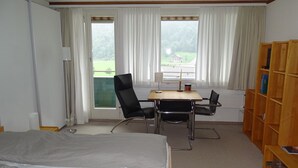 A hotel room with a bed, a desk, two chairs, a bookshelf, and a window with curtains. - Parkweg 9/602 Appartement/Fewo 2-Bettwohnung by Interhome (Engelberg)