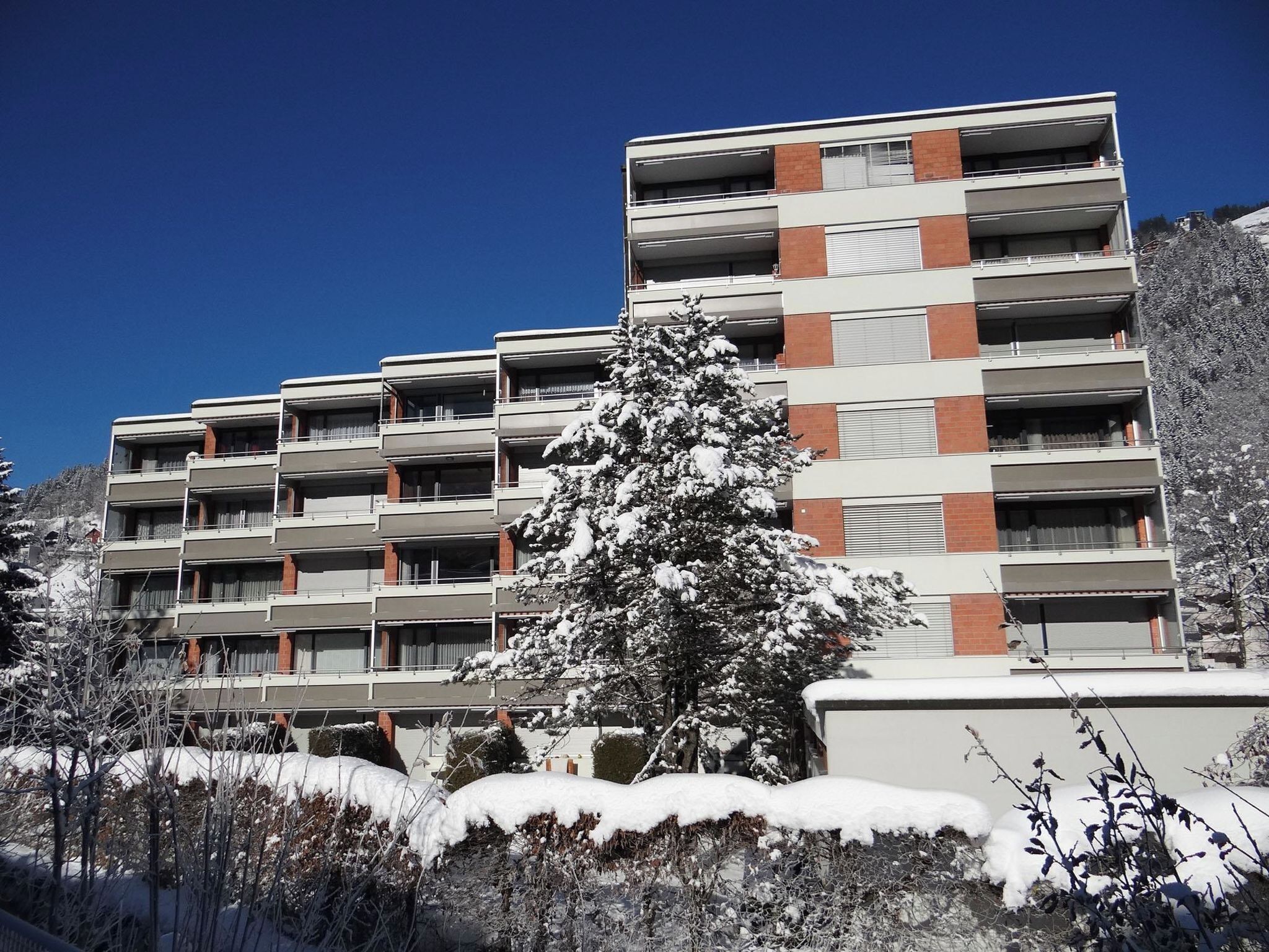 A multi-story building with a modern architectural style, featuring a mix of brick and white exterior walls, and balconies on each floor.