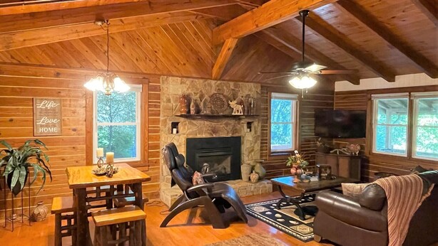 A cozy cabin interior with a stone fireplace, wooden furniture, and a television. - Grumpy Bear Cabin-Hot Tub-Pet Friendly (Murphy)