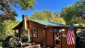 A rustic log cabin with a stone chimney, a wooden porch, and an American flag. - Grumpy Bear Cabin-Hot Tub-Pet Friendly (Murphy)