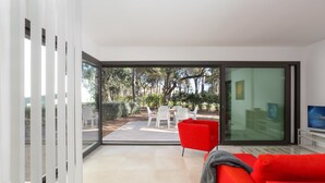 A modern living room with a red sofa, a TV, and a glass door leading to an outdoor patio with white chairs and a table. - 4 Bedroom Modern House, Llafranc, Costa Brava (Llafranc)
