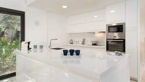 A modern kitchen with white cabinetry, a stainless steel oven, and a large island with blue cups. - 4 Bedroom Modern House, Llafranc, Costa Brava (Llafranc)