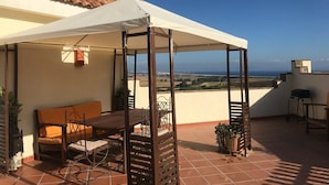 En overdækket terrasse med et bord, stole, en sofa og en grill.