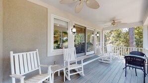 Eine überdachte Veranda mit weißen Stühlen und einem Tisch, großen Fenstern und Deckenventilatoren.
