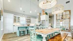 A spacious kitchen with white cabinetry, a wooden dining table, and teal chairs. - Sweet & Salty - Hot Tub, Across from Jetty, Best Ship Watching! (Surfside Beach)