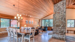 Un vaste salon doté d’un plafond en bois, d’un mur d’accent en pierre et de grandes fenêtres offrant une vue sur l’extérieur.