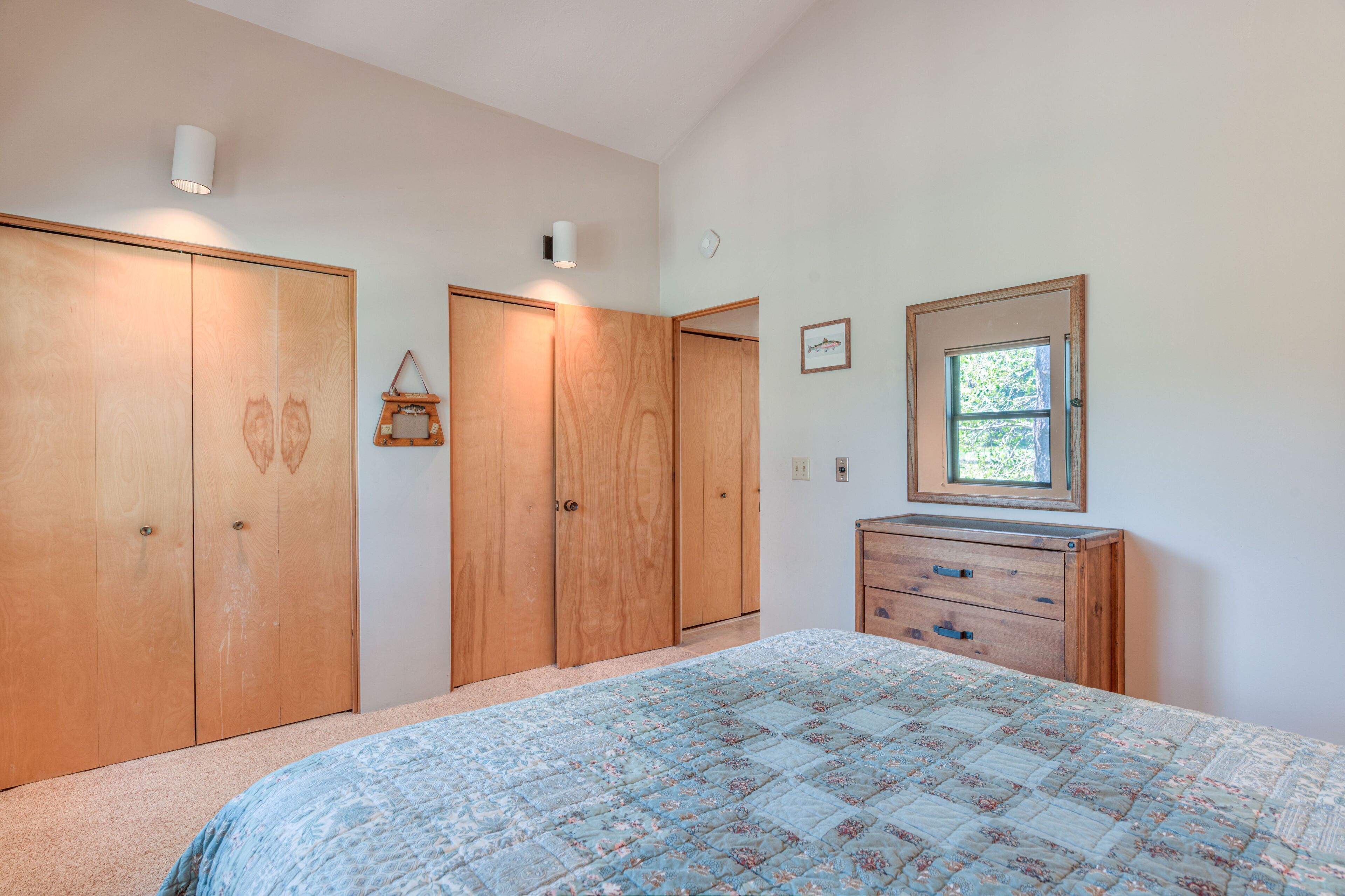 A bedroom with a bed, wooden wardrobe, dresser, and a small window.
