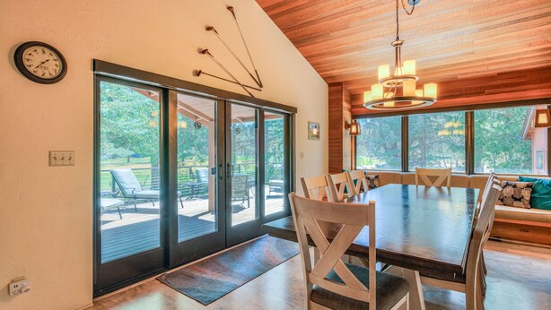 Un espace repas comprenant une grande table, des chaises et un lustre. Des portes-fenêtres coulissantes donnent sur une terrasse extérieure aménagée avec du mobilier.