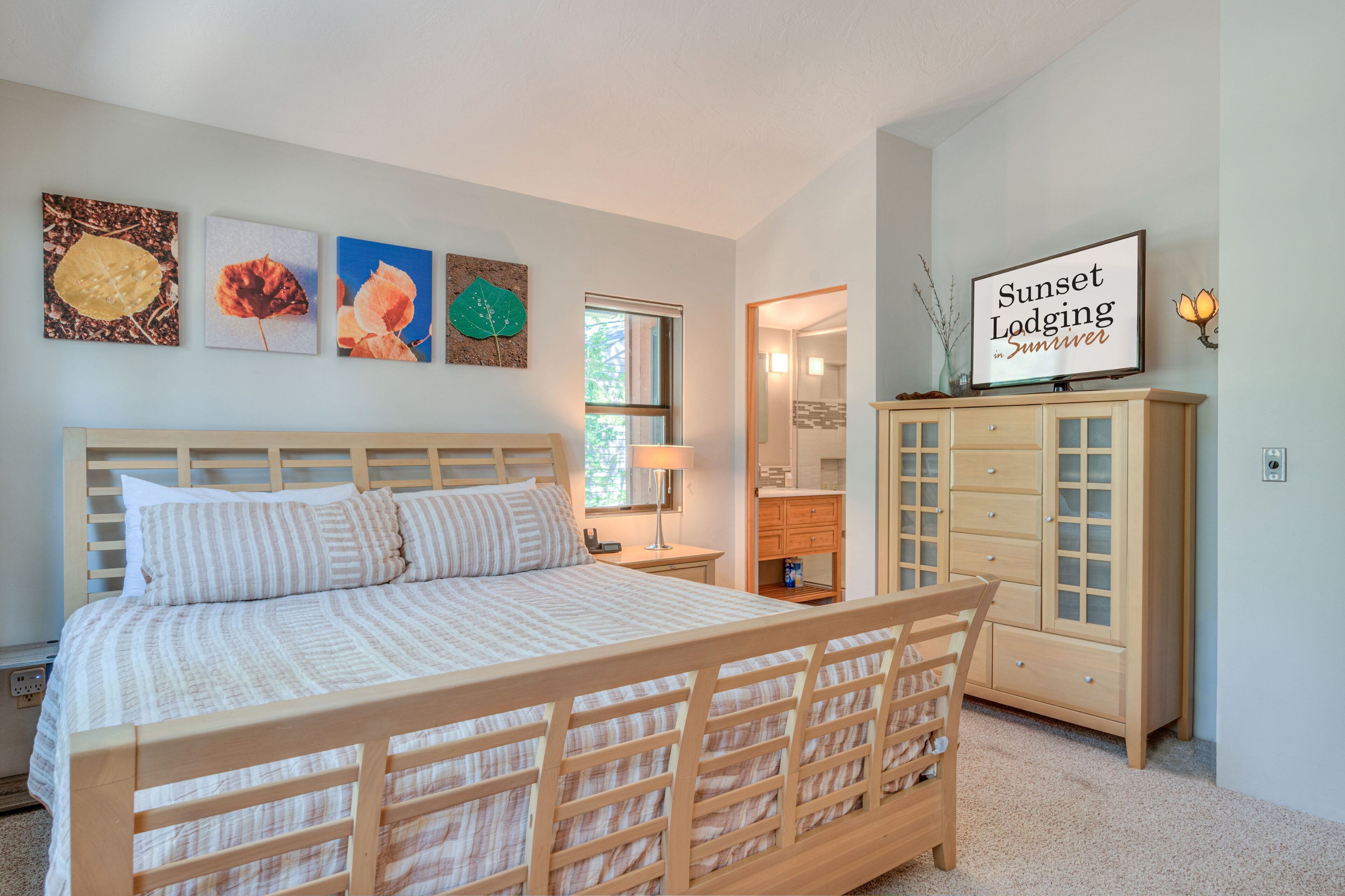 Quarto com cama de madeira, mesa de cabeceira, cômoda e obras de arte nas paredes.