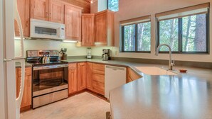 Une cuisine moderne dotée de meubles en bois, d’appareils électroménagers en acier inoxydable et de grandes fenêtres offrant une vue sur l’extérieur.